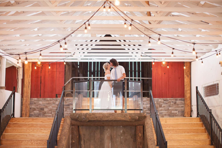 The couple kissing beneath string lights in the barn