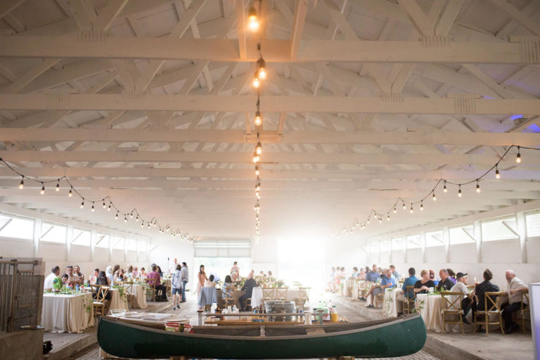 Guests at long tables in the white barn under strings of lights