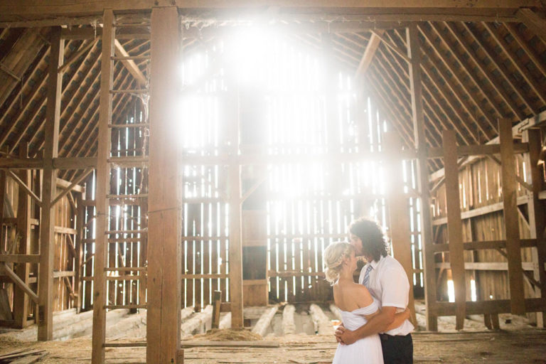 Sunlight streaming through the timber barn walls behind the couple