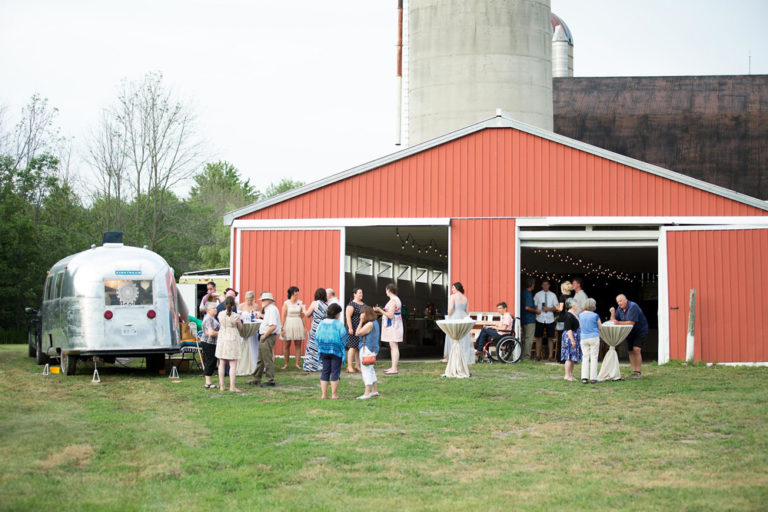 Guests outside the red barn beside a vintage trailer